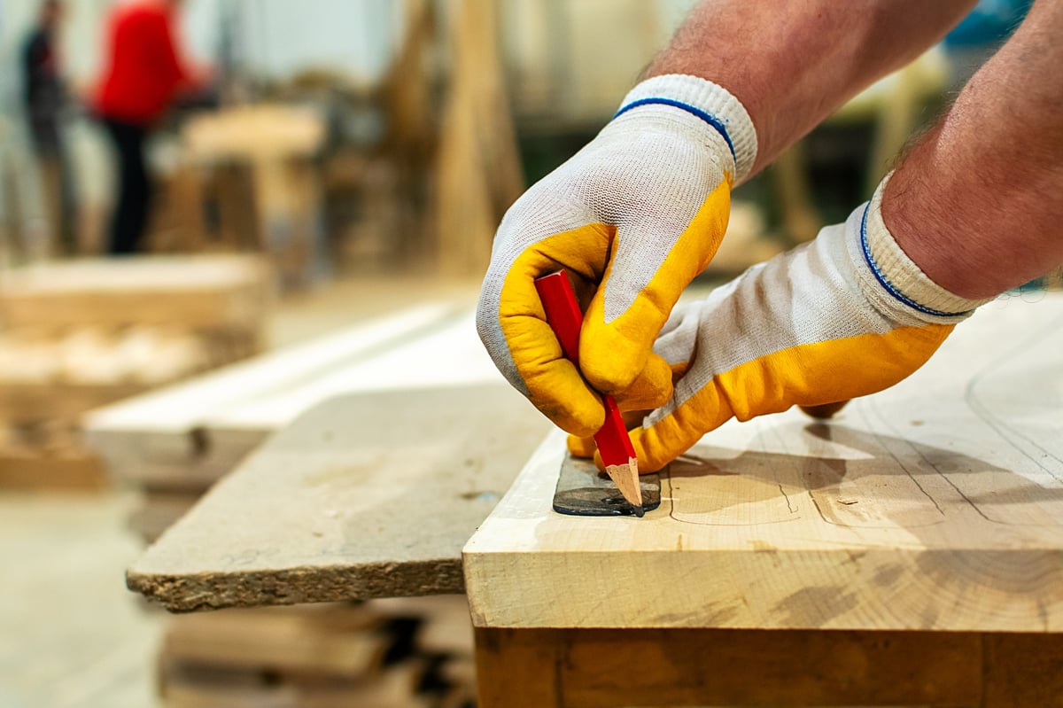 Close-up of a skilled carpenter wearing protective gloves, carefully marking a wooden plank with a pencil before cutting